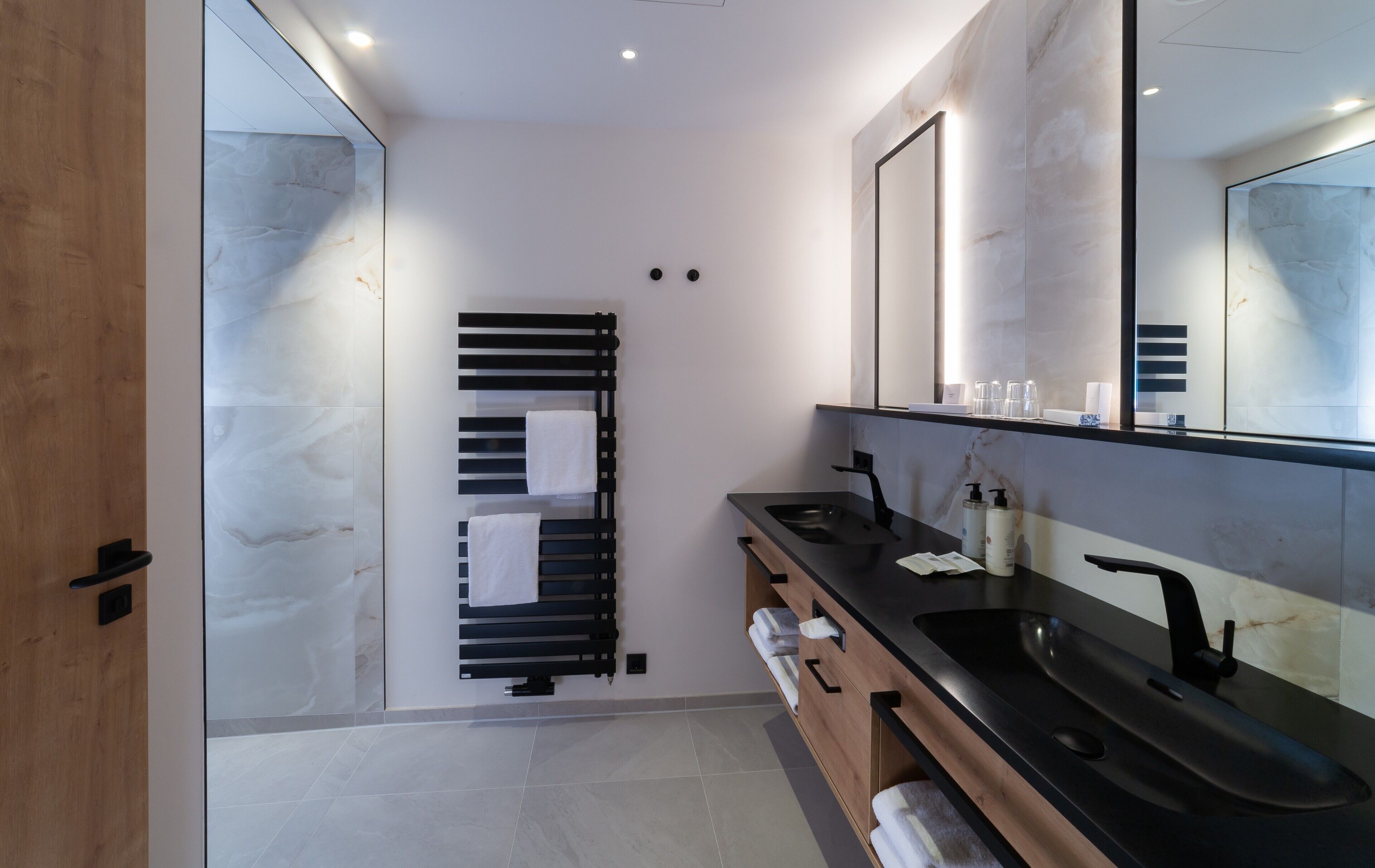 Un baño moderno con un lavamanos negro, un espejo grande y un perchero para toallas.