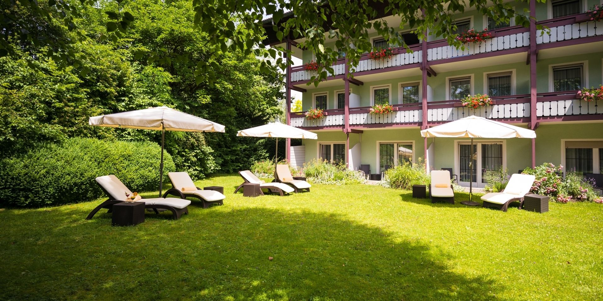 Een hotelbinnenplaats met meerdere lounge stoelen en parasols, omgeven door weelderige begroeiing en een meerlaags gebouw met balkons.