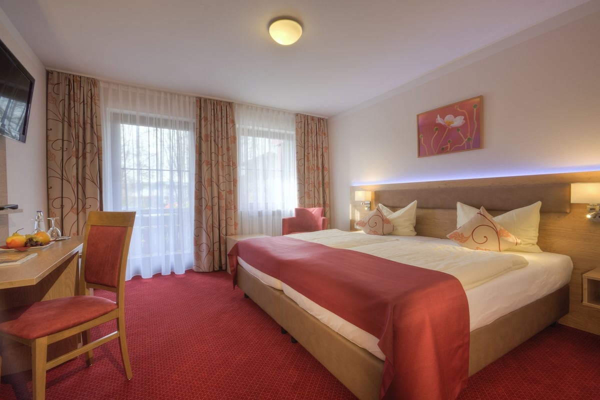 A hotel room with a large bed, a desk with a chair, and a television on the wall.