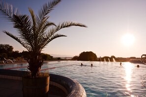 Ein Swimmingpool mit einer Palme im Vordergrund, umgeben von Liegestühlen und einer entfernten Bergsicht.