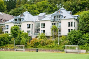 A row of modern, multi-story buildings with balconies and large windows, surrounded by lush greenery.