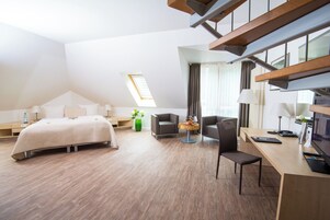 Una habitación de hotel moderna con una cama, un escritorio, una silla y una mesita. Cuenta con una ventana con cortinas y un tragaluz.