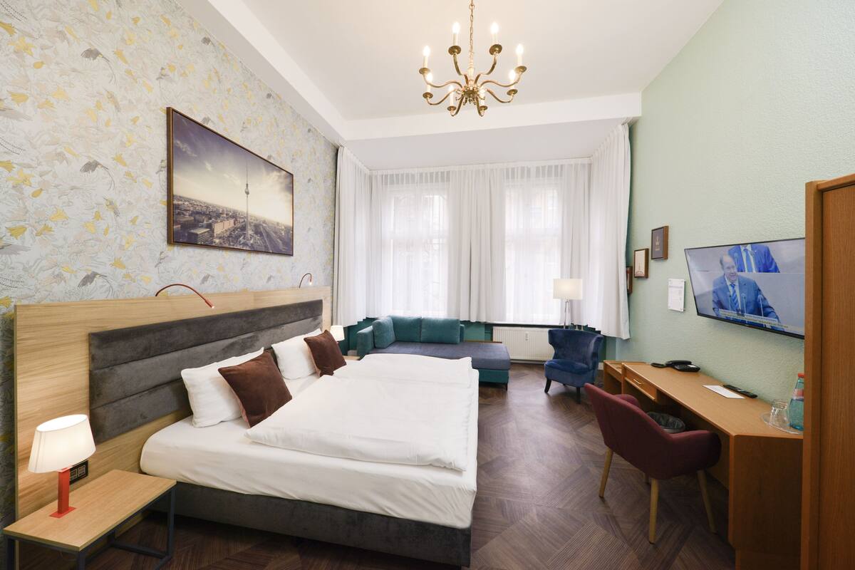 Ein Hotelzimmer mit Bett, Schreibtisch, Stuhl, Fernseher und einem Fenster mit Vorhängen.
