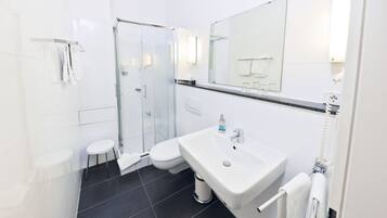 Ein modernes Badezimmer mit einer Duschkabine aus Glas, einem weißen Waschbecken und einem großen Spiegel.
