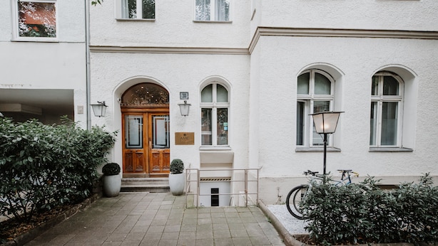 A white building with a wooden door, a sign reading "AMC", and a bicycle parked outside. - AMC Hotel - Schöneberg (Berlin)