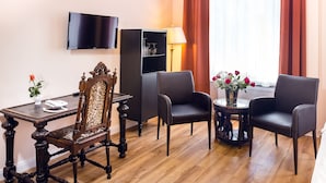 A room with a wooden table, two chairs, a television, a bookshelf, and a window with curtains. - AMC Hotel - Schöneberg (Berlin)