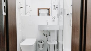A compact, modern bathroom with a white toilet, a small sink, and a glass shower enclosure. - AMC Hotel - Schöneberg (Berlin)