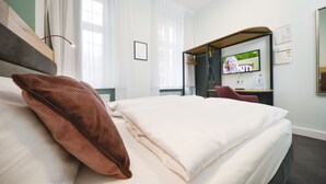 A hotel room with a bed, a television, a desk, and a chair. - AMC Hotel - Schöneberg (Berlin)