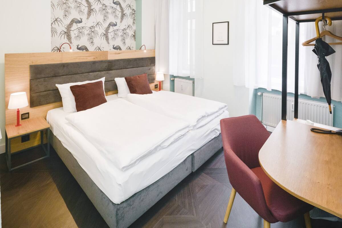 Ein Hotelzimmer mit einem großen Bett, einem Holzkopfschild, einem roten Sessel, einem Holztisch und einem an der Wand befestigten Kunstwerk.