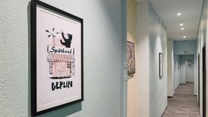 A hallway with framed artwork on the walls, a carpeted floor, and a light-colored wall. - AMC Hotel - Schöneberg (Berlin)