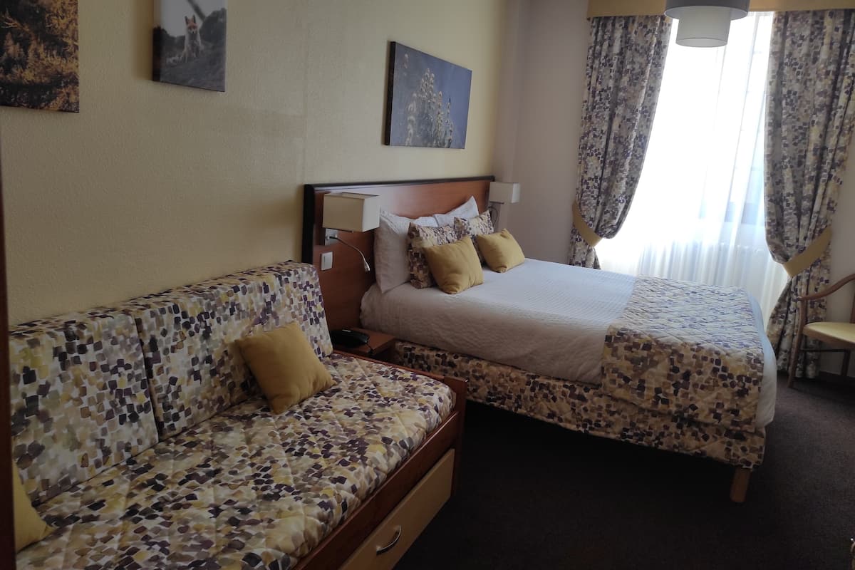 Une chambre d’hôtel avec un lit, un canapé, une table de chevet et une lampe.
