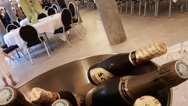 Een feestzaal met gedekte tafels voor een formeel evenement, een grote stenen zuil en een emmer champagneflessen.