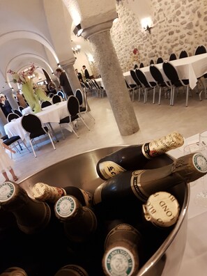 A banquet hall with tables set for a formal event, a large stone pillar, and a bucket of champagne bottles.