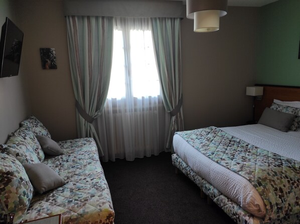 A hotel room with two beds, a sofa, a window with curtains, and a lamp.