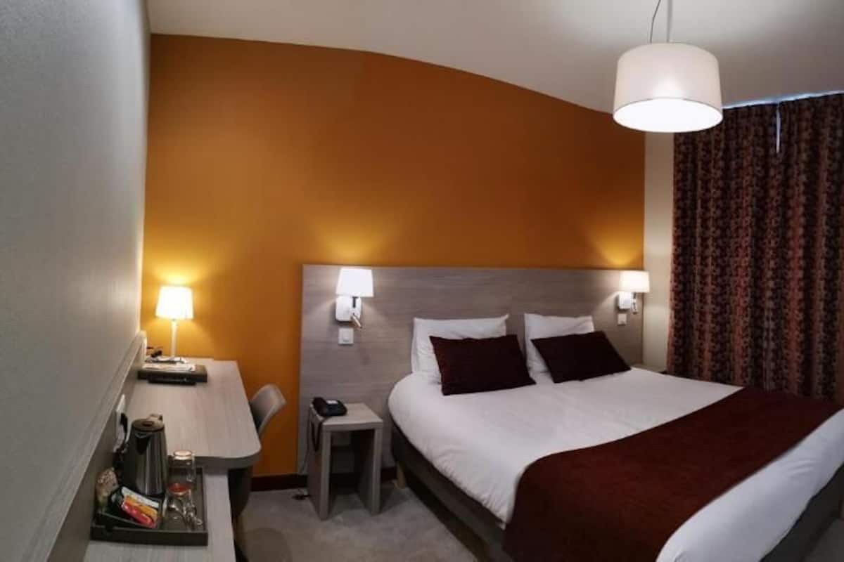 Une chambre d’hôtel avec un grand lit, des lampes de chevet, un bureau avec une lampe, une chaise et un téléviseur fixé au mur.