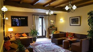Een gezellige woonkamer met een zithoek, een salontafel en een vloerkleed met een patroon. Er zijn twee wandlampen, een plafondventilator en een groot raam met gordijnen.