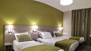 Een hotelkamer met twee bedden, een gebogen hoofdeinde, bedlampen en een raam met gordijnen.