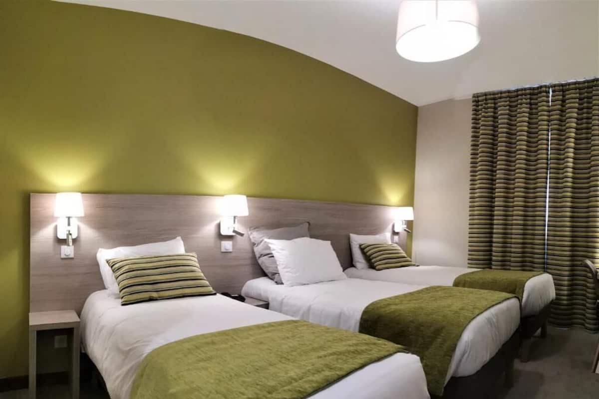 Une chambre d’hôtel avec deux lits, une tête de lit incurvée, des lampes de chevet et une fenêtre avec des rideaux.