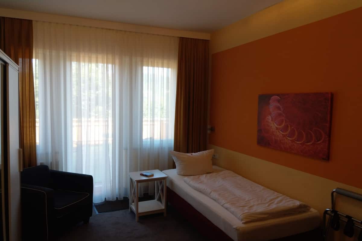 Ein Hotelzimmer mit Bett, kleinem Tisch, Stuhl und einem Gemälde an der Wand.
