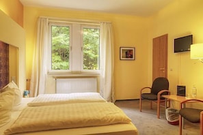 Una camera d'albergo con un letto, una scrivania, una sedia, una TV e una finestra con tende.