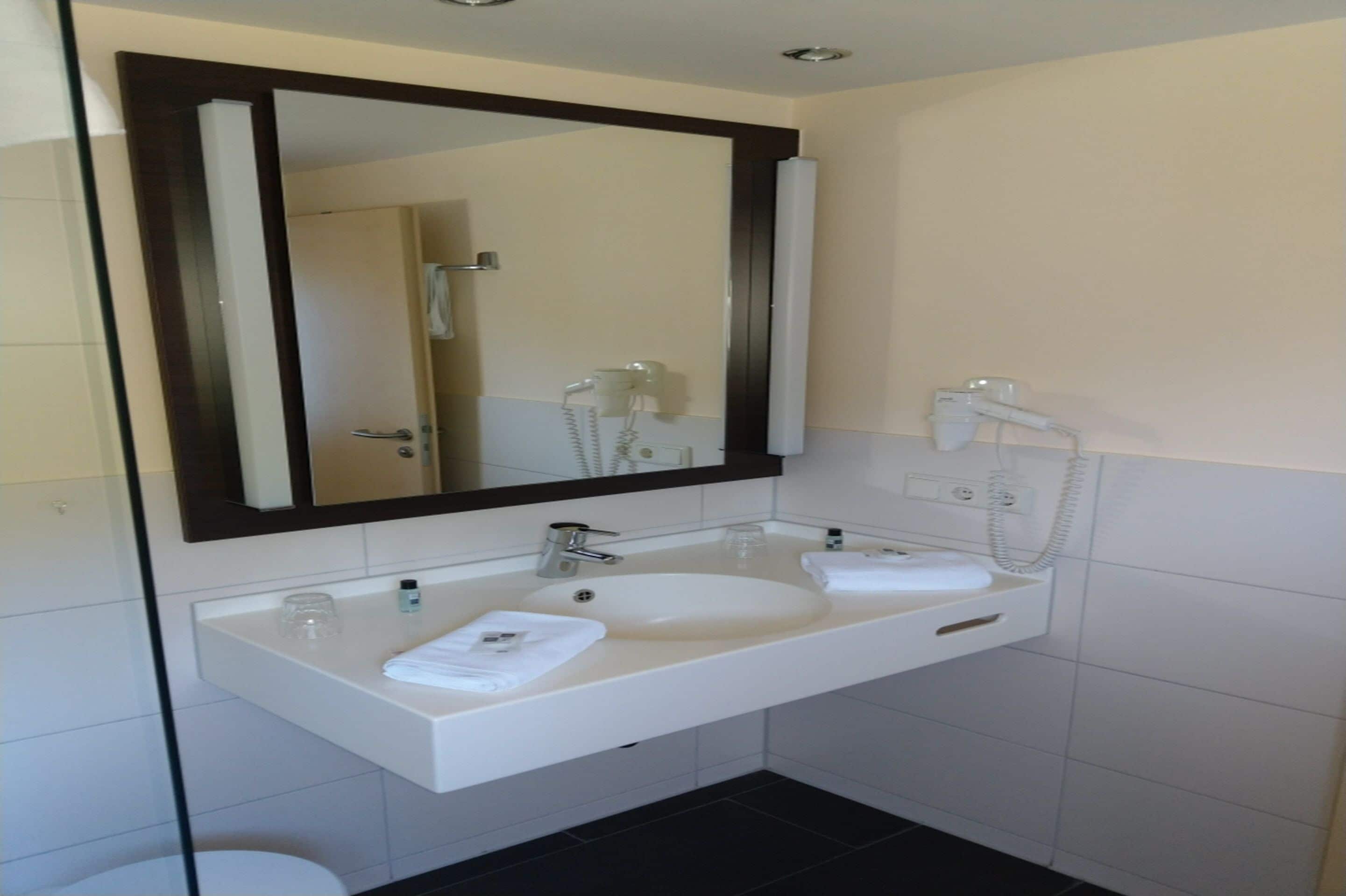 A modern bathroom with a large mirror, two sinks, and a towel rack.