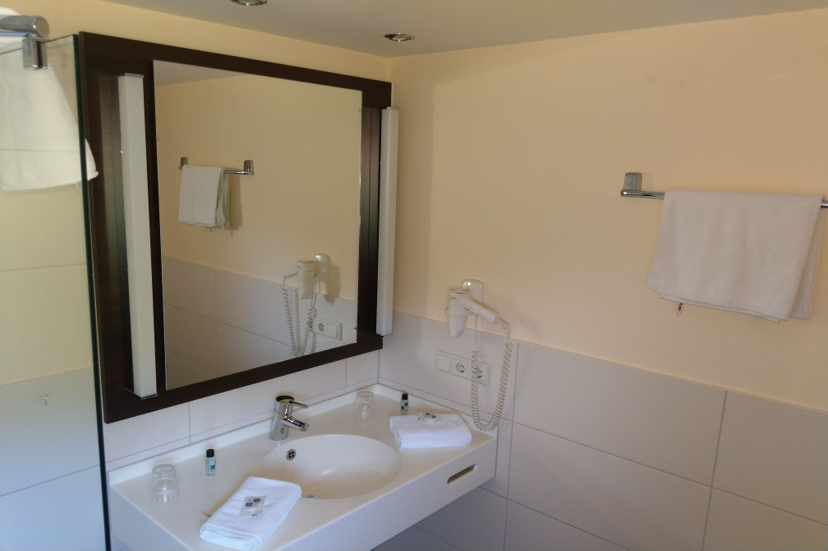 A bathroom with a large mirror, a sink, a towel rack, and a telephone.