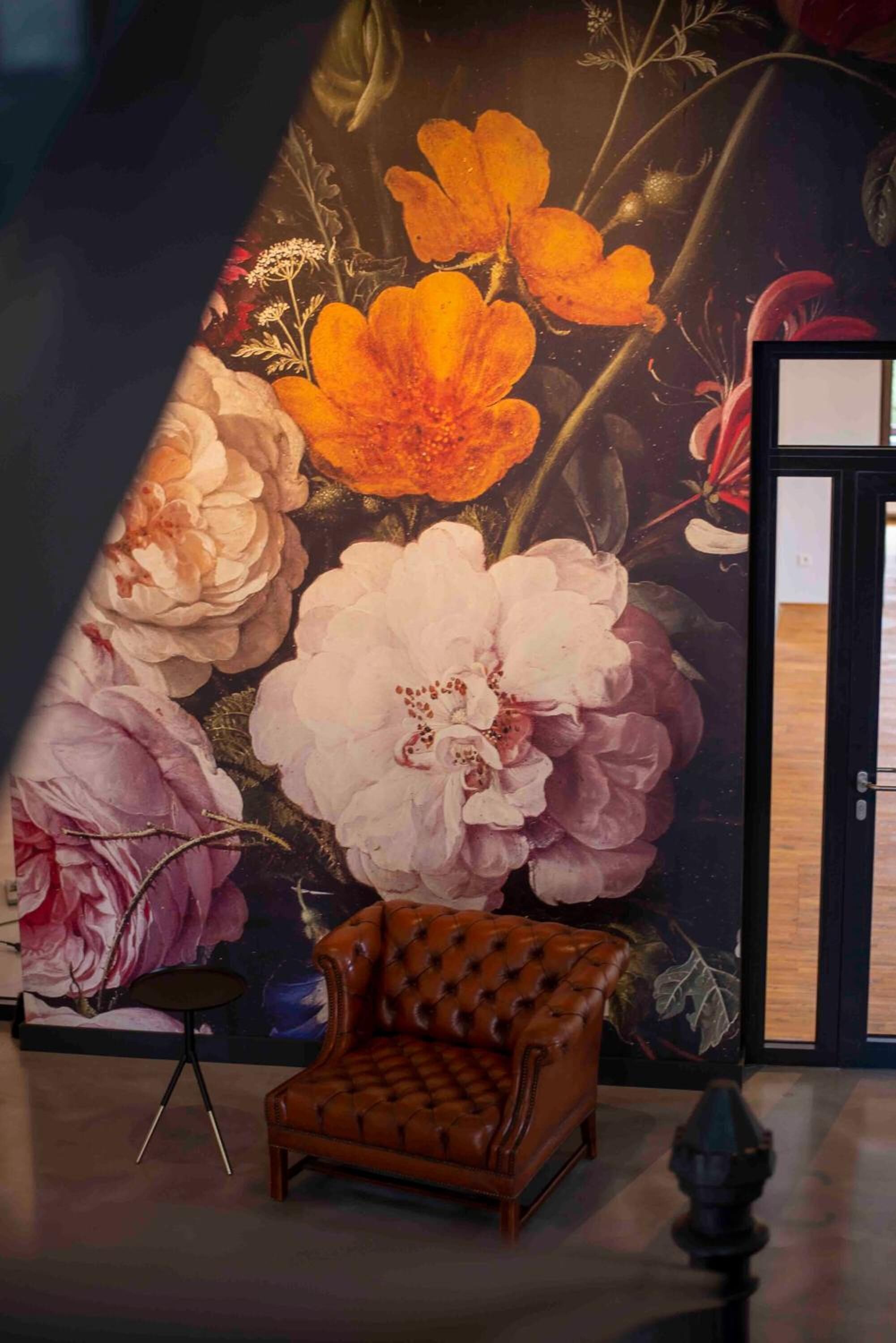 A room with a large floral mural on the wall, a leather armchair, and a small round table.