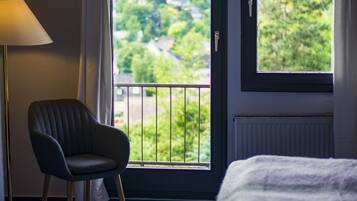 Ein Hotelzimmer mit Bett, Stuhl, Fenster und Blick ins Grüne sowie einer Lampe.