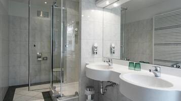 Un baño moderno con ducha envuelta en vidrio, dos lavamanos y un espejo grande.
