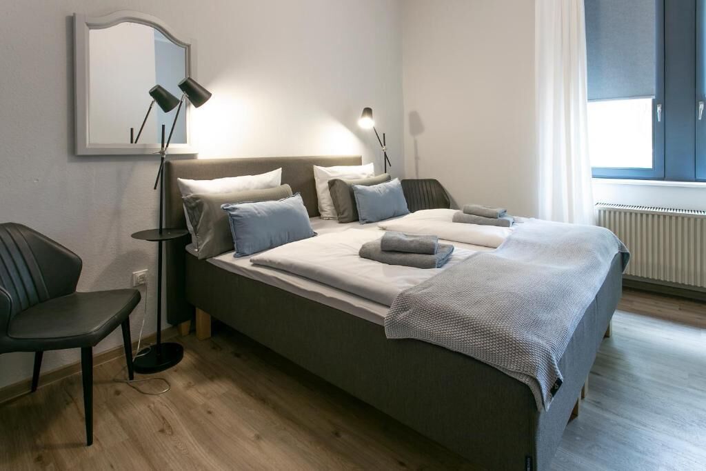 A modern hotel room with a large bed, bedside lamps, a chair, and a window with curtains.