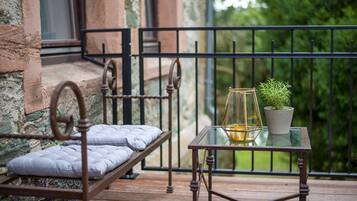 A balcony with a metal bed, a glass table with a plant, and a view of greenery.