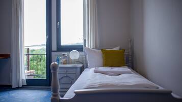 A bedroom with a bed, a bedside table, a window with curtains, and a view of greenery outside.
