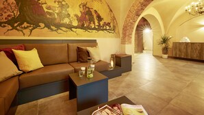 A modern interior with a curved wall mural, a seating area with cushions, a small table with a candle, and a reception desk in the background. - Schlosshotel Braunfels (Braunfels)
