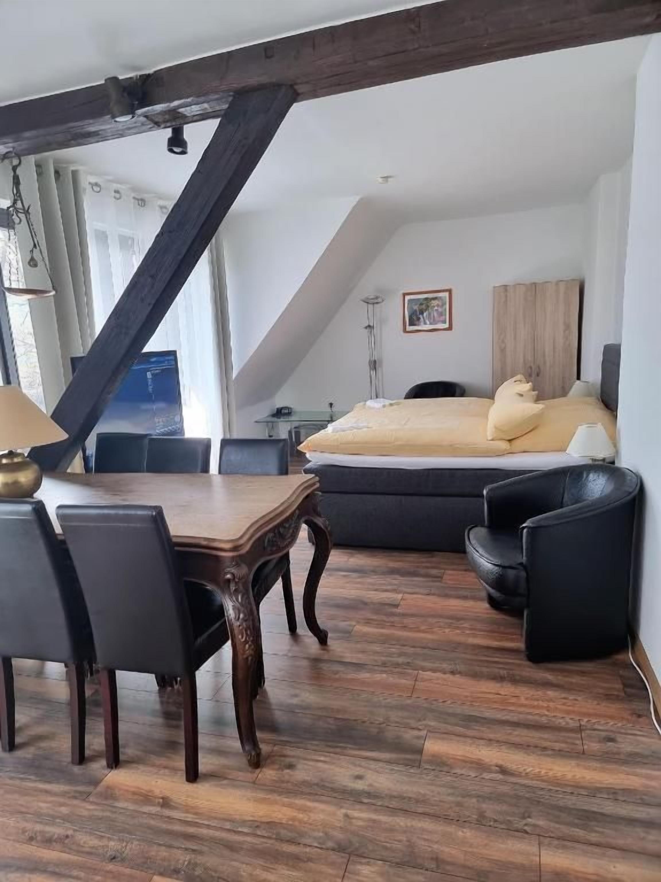 A room with a dining table, chairs, a sofa, and a bed.