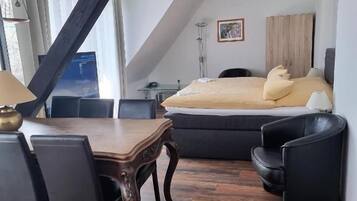 A room with a dining table, chairs, a sofa, and a bed.
