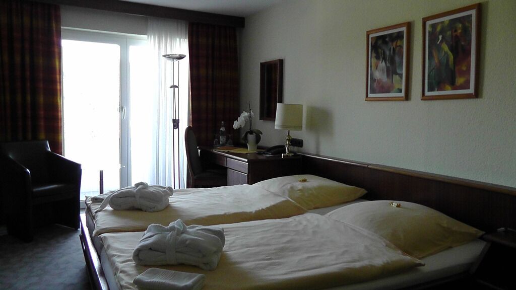 A hotel room with two beds, a desk, a chair, and a window with curtains.