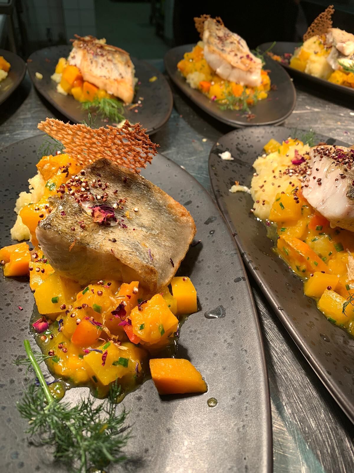 Un plat composé de poisson, de dés de mangue et d’un élément croustillant, peut-être un biscuit ou du pain, le tout agrémenté d’herbes et d’épices.