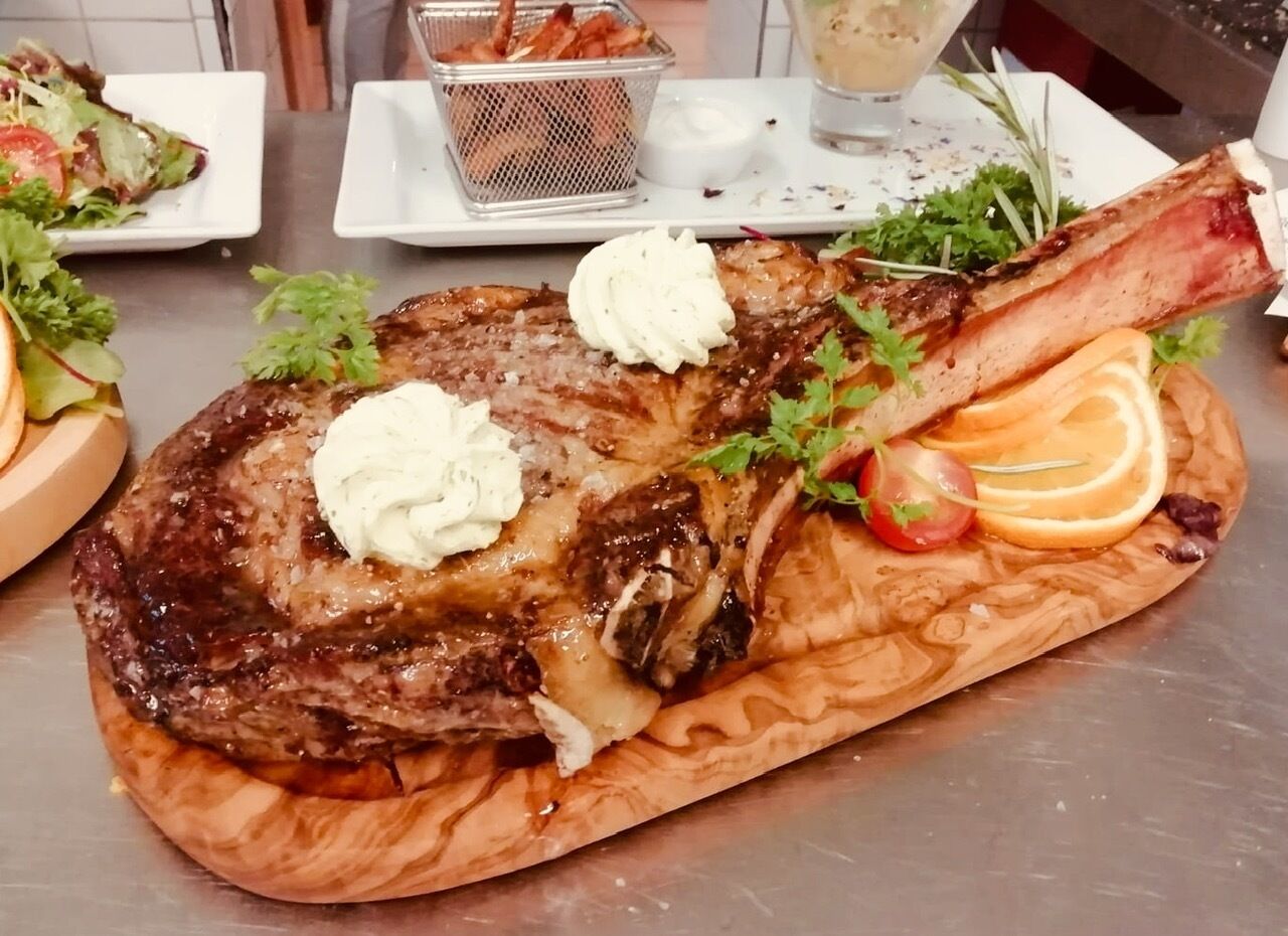 Un plato de carne con vegetales y una salsera pequeña sobre una tabla de madera.