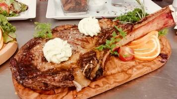 Un plato de carne con vegetales y una salsera pequeña sobre una tabla de madera.
