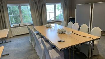 Et mødelokale med et langt bord, hvide stole, en projektor og store vinduer med gardiner.