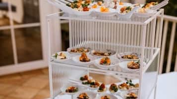 Un présentoir en verre à plusieurs niveaux, où sont exposés divers aliments, accompagné d’une pile d’assiettes blanches et d’une serviette en papier marron avec du texte.
