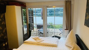 Une chambre d’hôtel avec un lit, une vue sur un lac et une terrasse aménagée avec du mobilier d’extérieur.