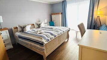Habitación de hotel con cama, escritorio, silla, lámpara y ventana con cortinas.