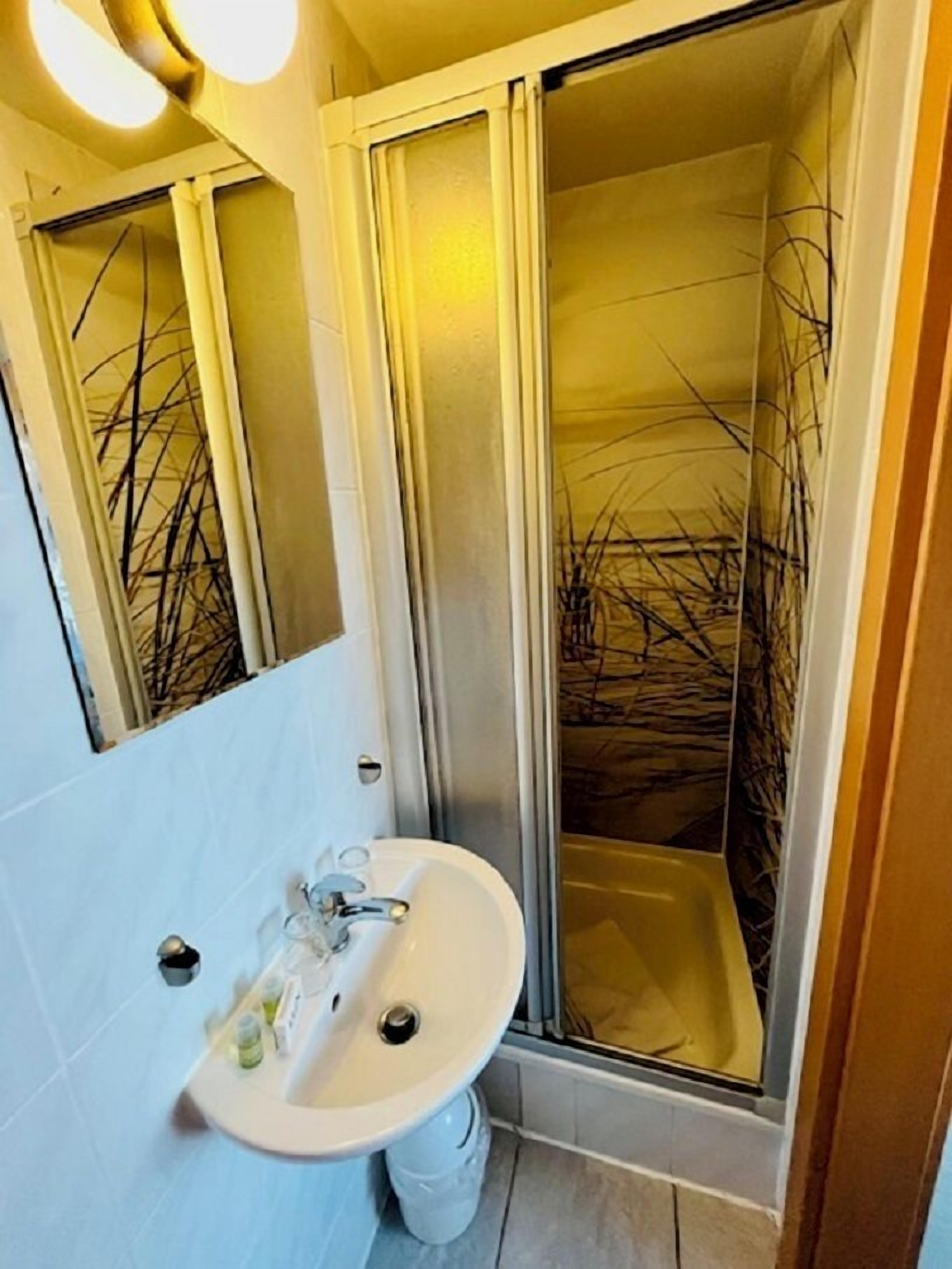 Casa de banho com lavatório branco, cabine de duche em vidro e espelho.