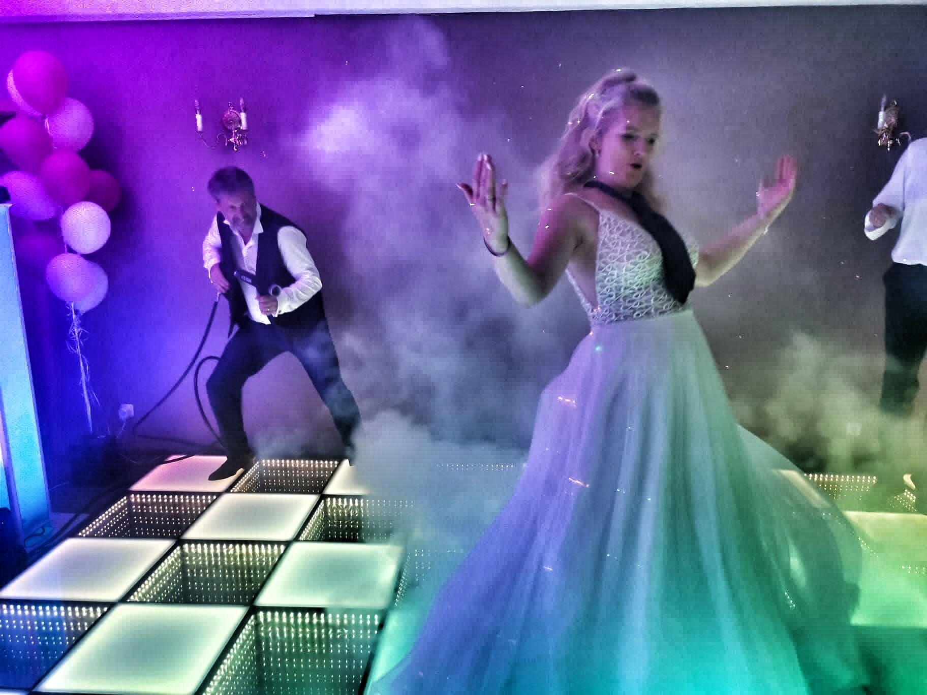 A woman in a white dress dancing on a stage with a man in a suit and another person in the background.