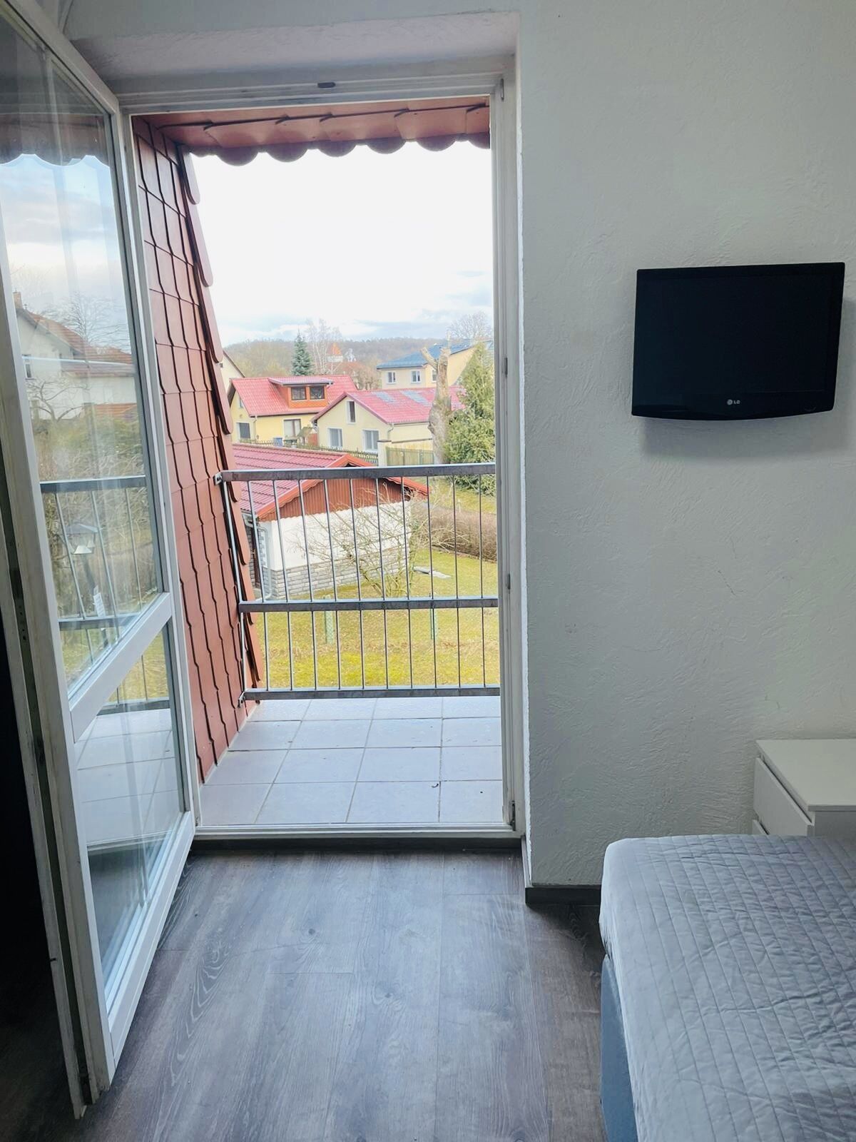 Un balcón con vistas a casas, un televisor montado en la pared y una cama con colcha.