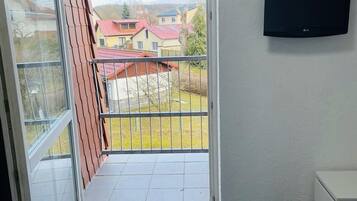 Un balcón con vistas a casas, un televisor montado en la pared y una cama con colcha.