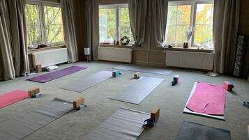 Una habitación amplia con ventanas grandes, colchonetas de ejercicio y cajas esparcidas en el suelo.