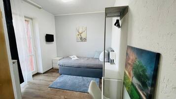 A small, well-lit bedroom with a bed, bedside table, and a painting on the wall.