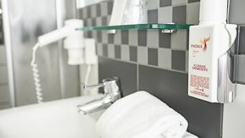 Un baño con estante de vidrio que contiene artículos de aseo, una toalla y un dispensador de crema PHONIX.